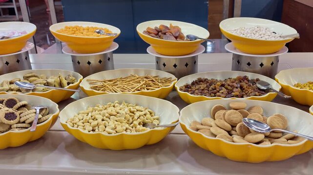 Camera slowly panning across a hotel dessert buffet counter featuring various yellow bowls filled with cookies, biscuits, nuts, dried apricots, raisins, and sweet snacks.