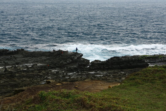 Fishermen stand on the rocky shore by the sea.
