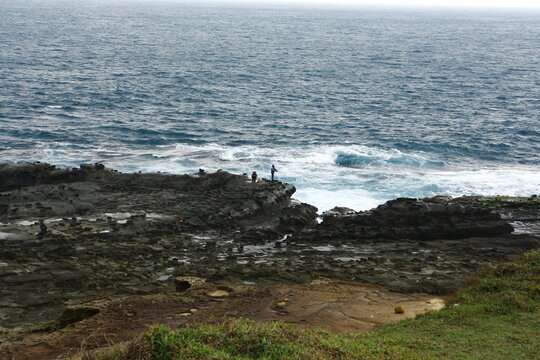 Fishermen stand on the rocky shore by the sea.