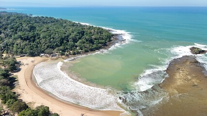 Aerial drone view of a curved tropical beach bay, turquoise water rolling into white foamy waves against golden sand under a clear sky, capturing a peaceful, perfect for travel and nature themes. © rifnaldi