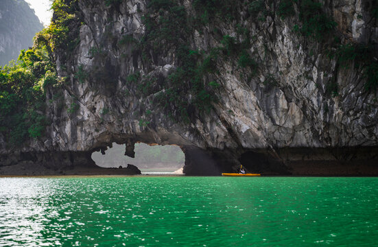 Kayaker paddling through a natural rock arch on emerald water