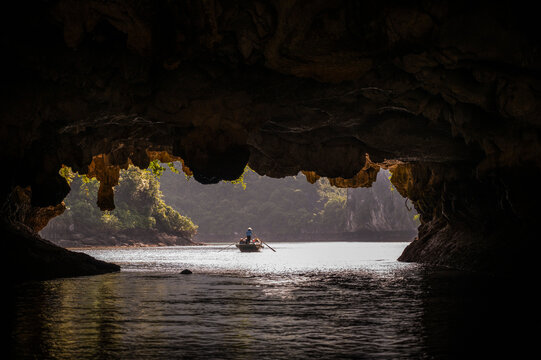 A person rows a boat out of a dark sea cave