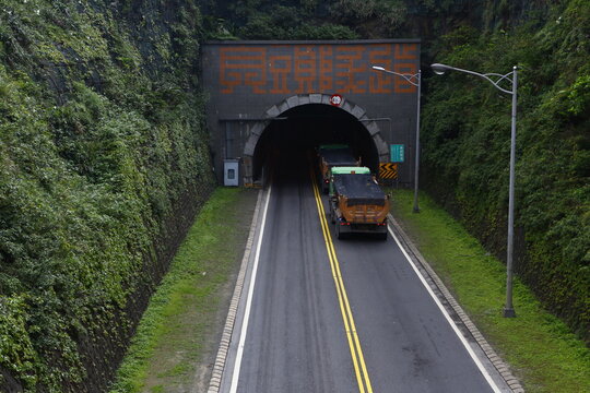 Heavy trucks enter Bitou tunnel cut through green mountains.
