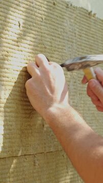 close-up view of hand positioning white plastic anchor into round hole of beige fibrous insulation panel site