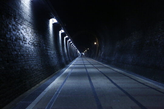 Lights illuminate a dark tunnel leading toward the bright exit.