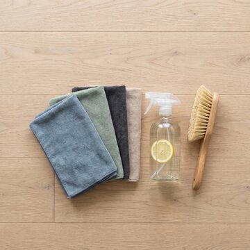 Assortment of sustainable cleaning products, including microfiber cloths, a natural spray cleaner with lemon, and a wooden brush, promoting environmental responsibility and home care