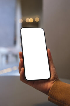 Vertical mockup image of a woman holding mobile phone with blank desktop screen in cafe