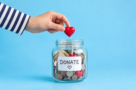 Hand Holding Red Heart Above Donation Jar Filled With Money for Charity Fundraising and Community Support
