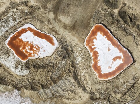 Saline ponds with ruddy algae growth and white salt deposits at the Skeleton Coast. Aerial view. Drone shot. Namib Desert, Dorob National Park, Namibia