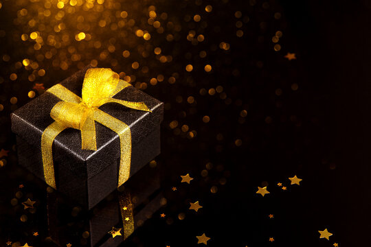 Black gift box with gold ribbon on dark festive background with glowing bokeh lights and copy space for Black Friday Christmas holiday and luxury promotion