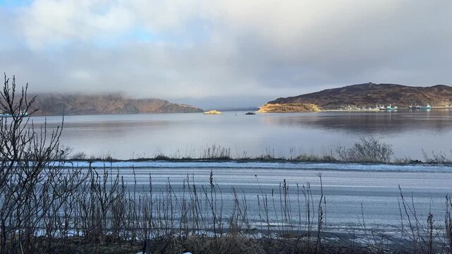 Slow panning shot of Captain's Bay's glassy waters with fog lowering over distant hills on a winter morning 