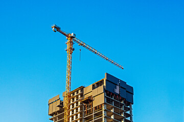 A construction crane near a tall, unfinished building against a blue sky. © Oleksandr Davydenko