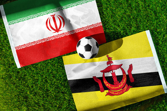 Iran vs. Brunei football match. National flags on green grass with soccer ball in the middle. Football background for international match.
