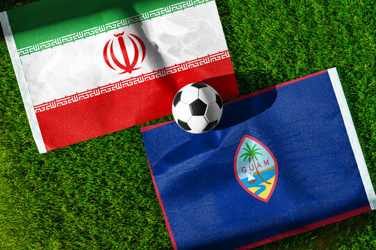 Iran vs. Guam football match. National flags on green grass with soccer ball in the middle. Football background for international match.