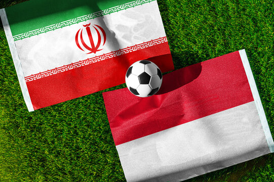 Iran vs. Indonesia football match. National flags on green grass with soccer ball in the middle. Football background for international match.