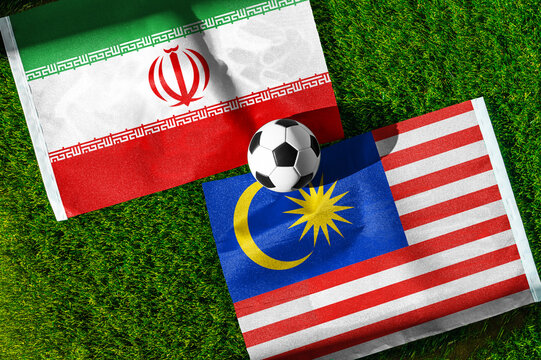 Iran vs. Malaysia football match. National flags on green grass with soccer ball in the middle. Football background for international match.