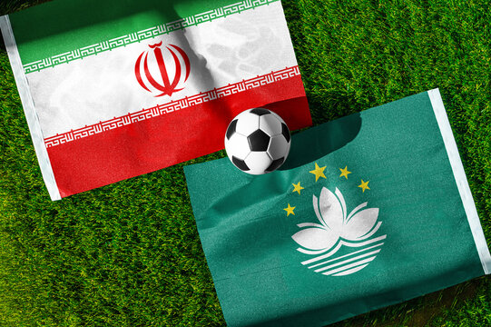 Iran vs. Macau football match. National flags on green grass with soccer ball in the middle. Football background for international match.