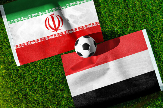 Iran vs. Yemen football match. National flags on green grass with soccer ball in the middle. Football background for international match.
