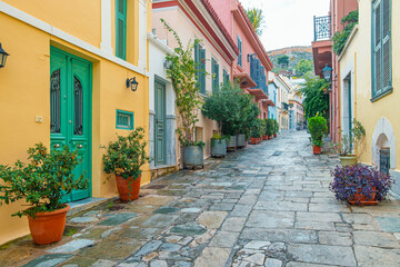 Obraz premium Stone paved street with colorful traditional houses, green doors and potted plants in Athens, Greece. Mediterranean architecture, European city travel, urban tourism and charming historic streetscape