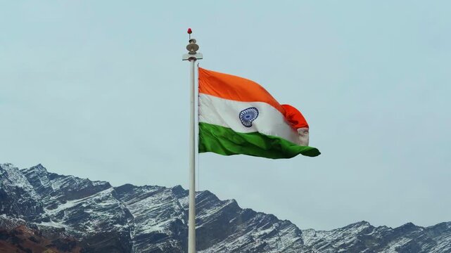 4K shot of Indian tricolor flag waving in front of snowy Himalayan mountain peaks as seen from Manali in Himachal Pradesh, India during the winter season. Flag of India waves in the Himalayas.