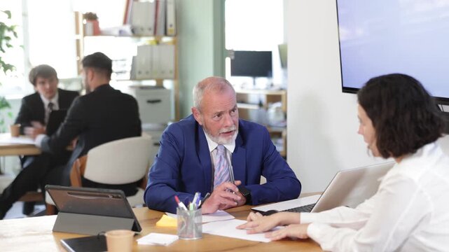 Professional senior man bank employee talking and signing loan agreement with young woman client in modern bank office 