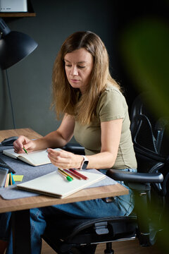 Woman choosing colored pencil at home office desk