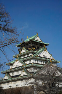 Osaka Castle tower with golden ornaments against clear blue sky, vertical view