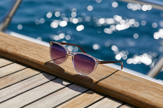 Beautiful and intricate composition showing premium UV protective sunglasses on a yacht deck with sparkling blue sea in the background, luxurious outdoor lifestyle, bright natural sunlight, minimalist