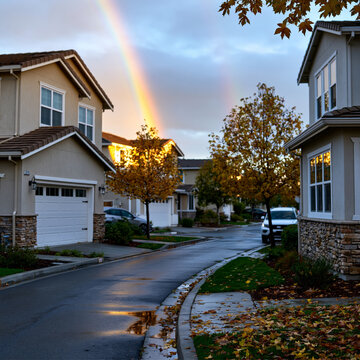 Twin spiral rainbows above a luxury suburban neighborhood with modern homes and landscaped gardens, clean composition, bright natural light, commercial real estate aesthetic,, perfect for modern