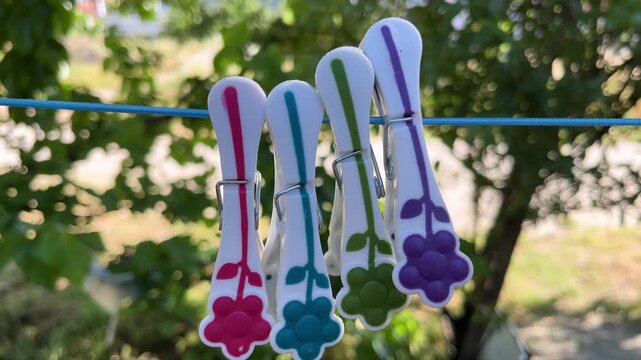 Colorful plastic flower shaped clothespins hanging on a clothesline gently swaying in the wind on a sunny day in a garden