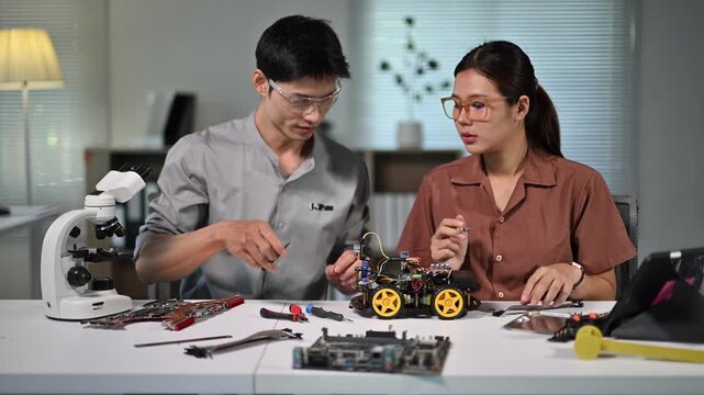 Two women working on electronics project with miniature vehicle and tools in a modern workspace