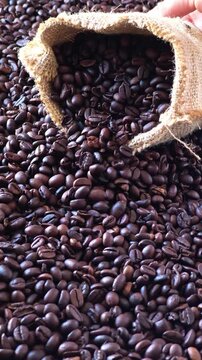 Close up of a burlap sack spilling aromatic roasted brown coffee beans over a dense background of freshly processed coffee.