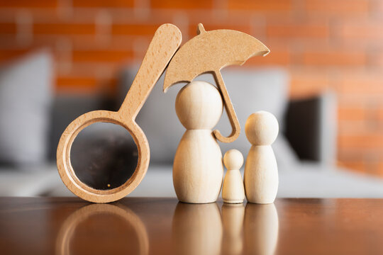 Family insurance audit and healthcare review concept with wooden peg doll figures under umbrella beside magnifying glass on table for domestic protection assessment and policy verification.