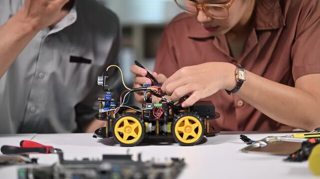 Two People Assembling and Testing a Small Remote-Controlled Robot on a Table