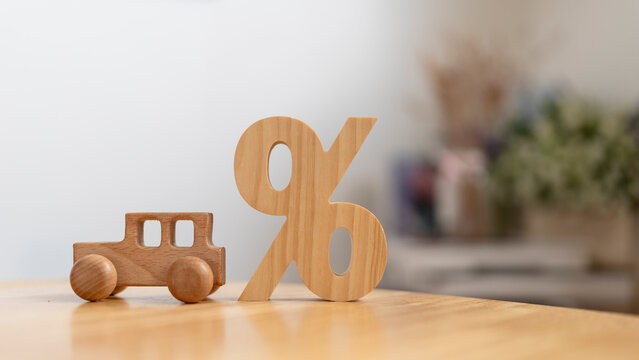 Auto loan interest rate and car finance discount concept with miniature wooden automobile beside percent symbol on table for vehicle leasing promotion, credit calculation and insurance cost.