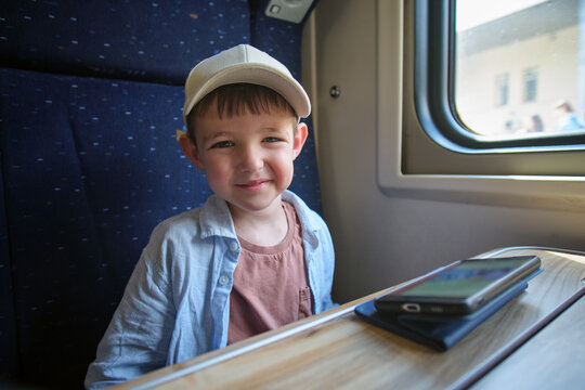 Little boy child sitting by window in train carriage during rail trip. Smiling kid passenger looking at camera. Travel lifestyle, railway transport journey and vacation experience.