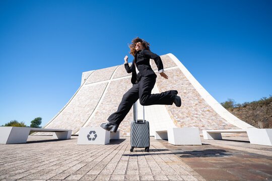 White female professional jumping with luggage
