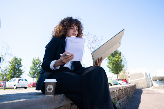 White woman writing notes and holding laptop outdoors