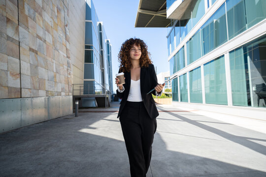 Businesswoman walking outdoors with coffee and folder in office area