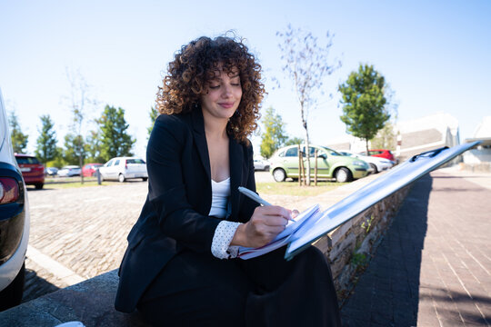 Businesswoman writing notes outdoors in urban car park in a park