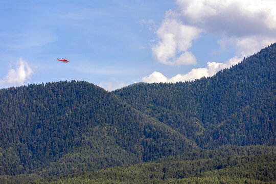 red medical emergency helicopter flying over green mountains