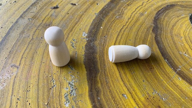 Two wooden peg figures arranged on a textured surface, symbolizing interaction, comparison, or social concepts