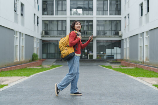 Student with backpack walking on university campus using phone