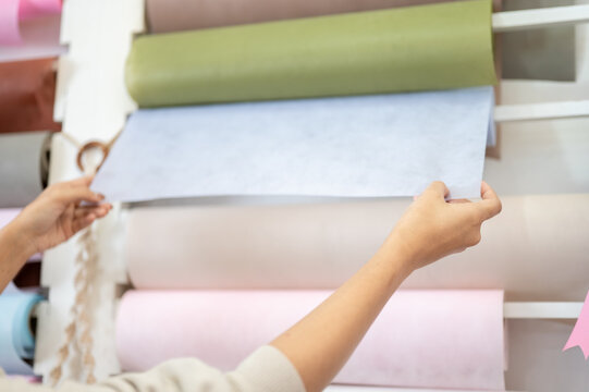 hands selecting light blue wrapping paper roll from craft shop shelf