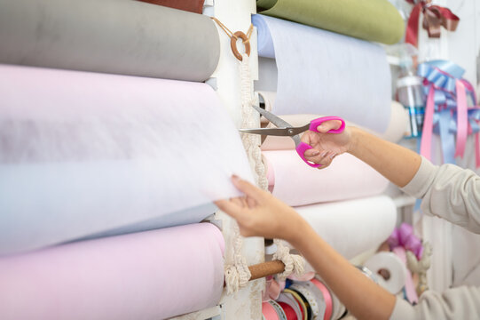 Close up of woman's hands cutting white wrapping paper roll with pink scissors in craft shop