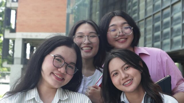 Portrait group cheerful asian male and female students carrying backpacks and textbooks stand smiling and waving at the camera in front university building ready begin their university studies.
