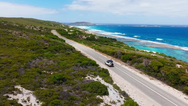 A car driving along the Esperance coast with the Ten Mile Lagoon in the background, filmed with a drone.