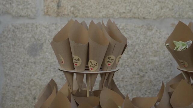 Rows of folded cones await guests on a tiered holder against a rough granite wall, one heart sticker on each, filled cones waiting behind