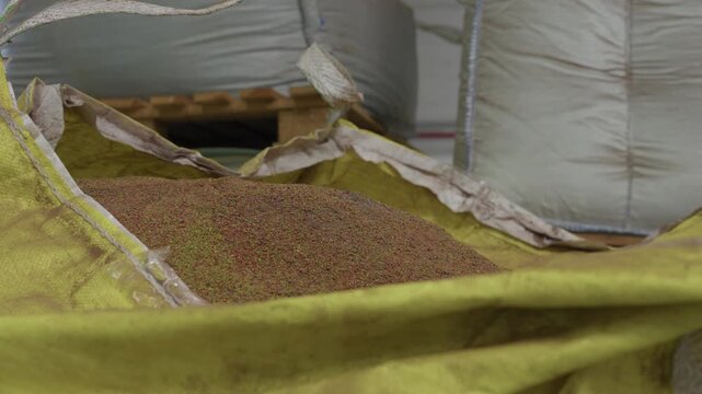 Fine recycled granulate resting in the liner of an opened yellow bulk bag at a plastics processing plant, further filled bags and a pallet behind