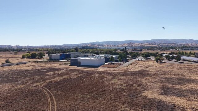 Panning aerial shot revealing the Solano Community College campus in Vacaville, California, surrounded by dry fields and rolling hills under a clear blue sky on a sunny day